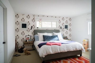 Open white bedroom with white flowered wallpaper and dog sitting on floor