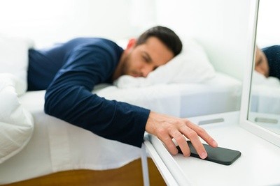 Man snoozing phone alarm in white room