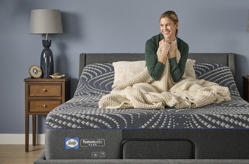 woman sitting on a mattress cuddled up with a blanket