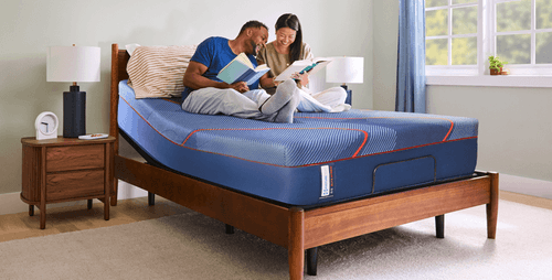 A man and a woman sitting on a posturepedic elite mattress while reading - mobile